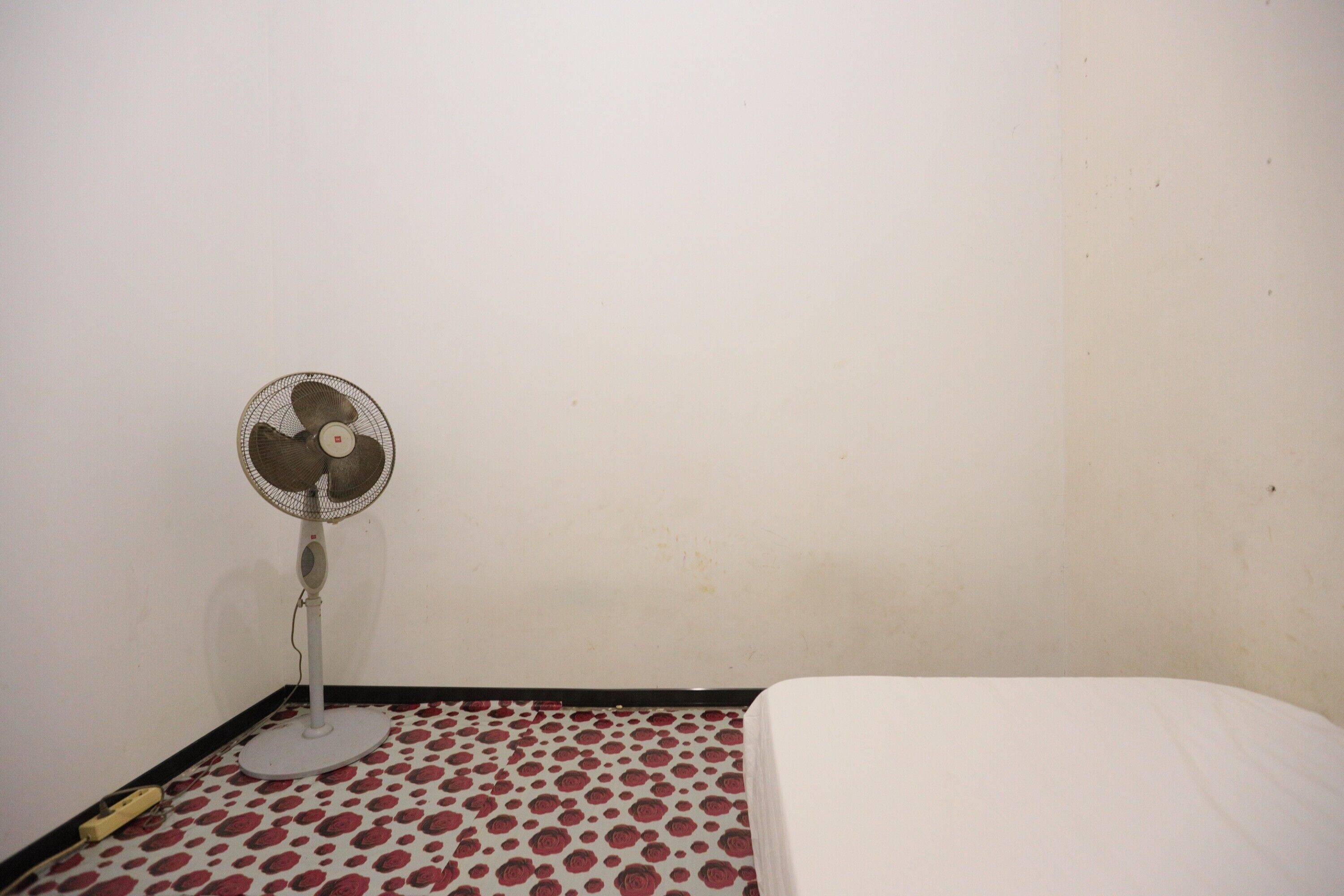 Una habitación con una cama, un ventilador de pie y un suelo estampado.