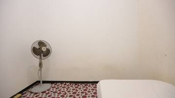 Una habitación con una cama, un ventilador de pie y un suelo estampado.