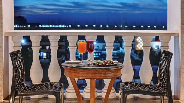 A balcony with a table set for two, featuring a glass top and two chairs. - Regenta Inn Motikhavdi Jamnagar  (Jamnagar)