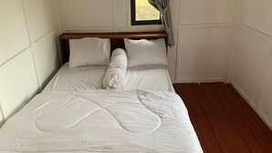 Cama bem arrumada com roupa de cama branca num quarto com piso de madeira e paredes brancas.