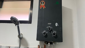 Um aquecedor de água preto com botões de controle e um chuveiro fixado na parede.