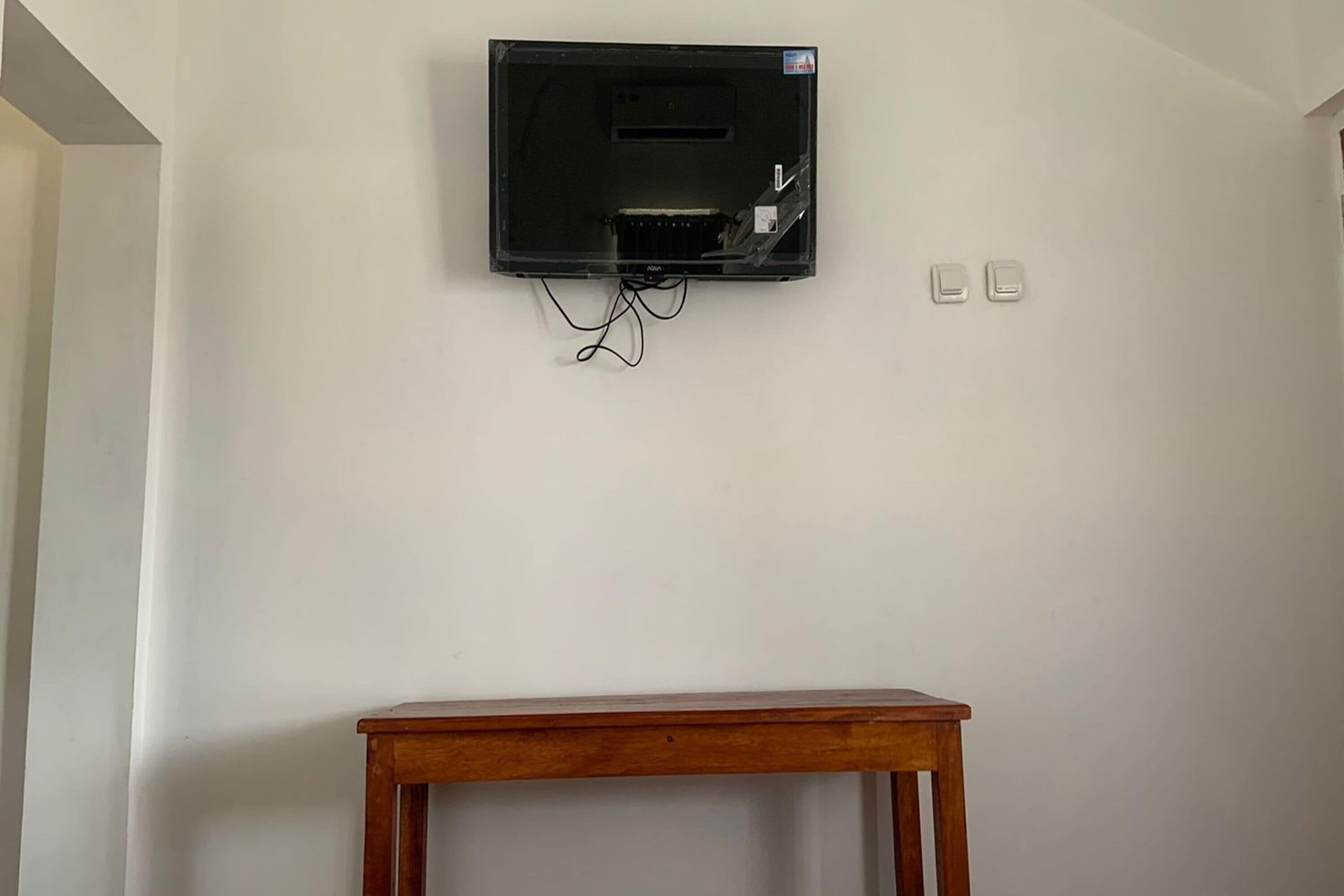 A television mounted on a plain wall with a wooden table in front.