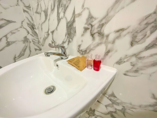 A white bathroom sink with a single faucet, a shower card, and two small bottles of liquid soap. - Goldsmith Bangkok Residence (Bangkok)