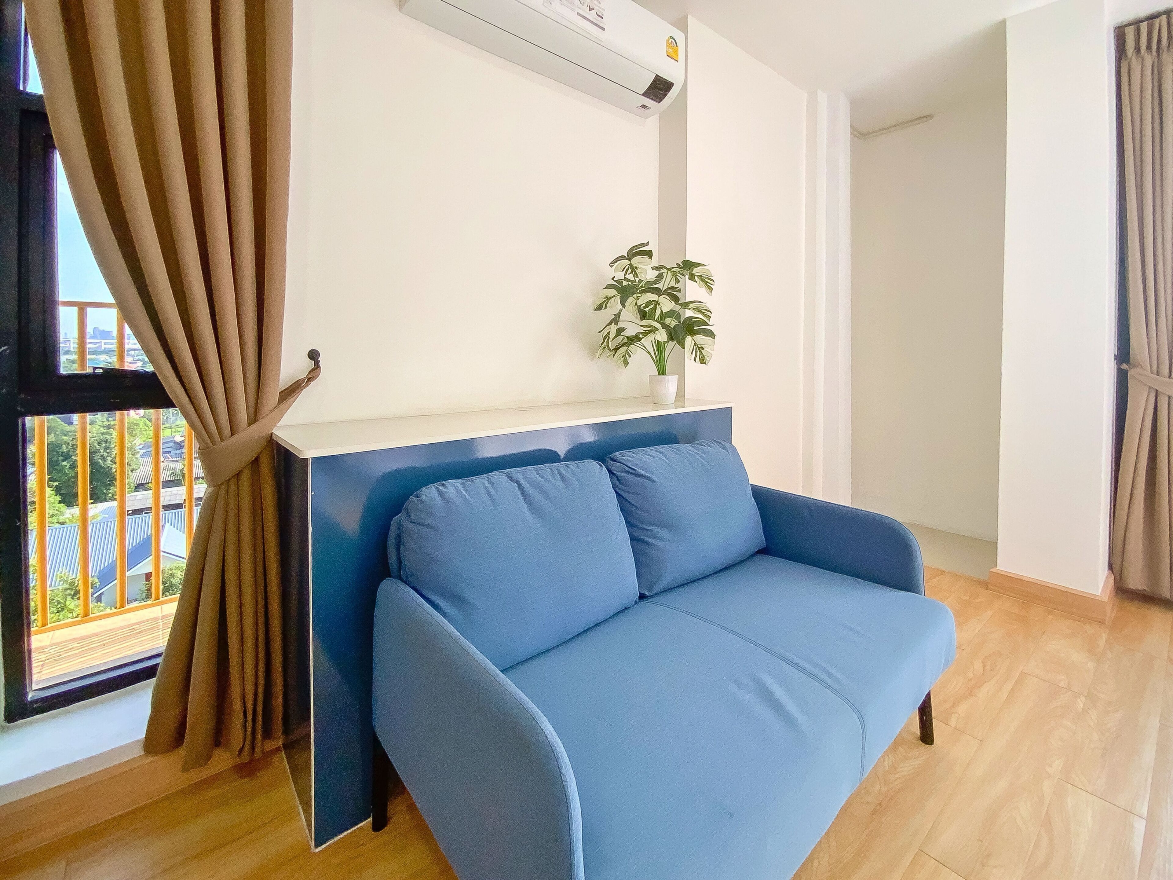 Una sala moderna con un sofá azul, una planta en maceta y una ventana con cortinas.