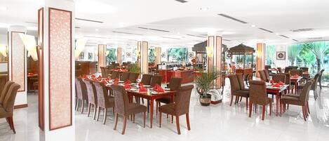 Un amplio comedor de hotel con varias mesas y sillas, ventanas grandes y una decoración moderna.