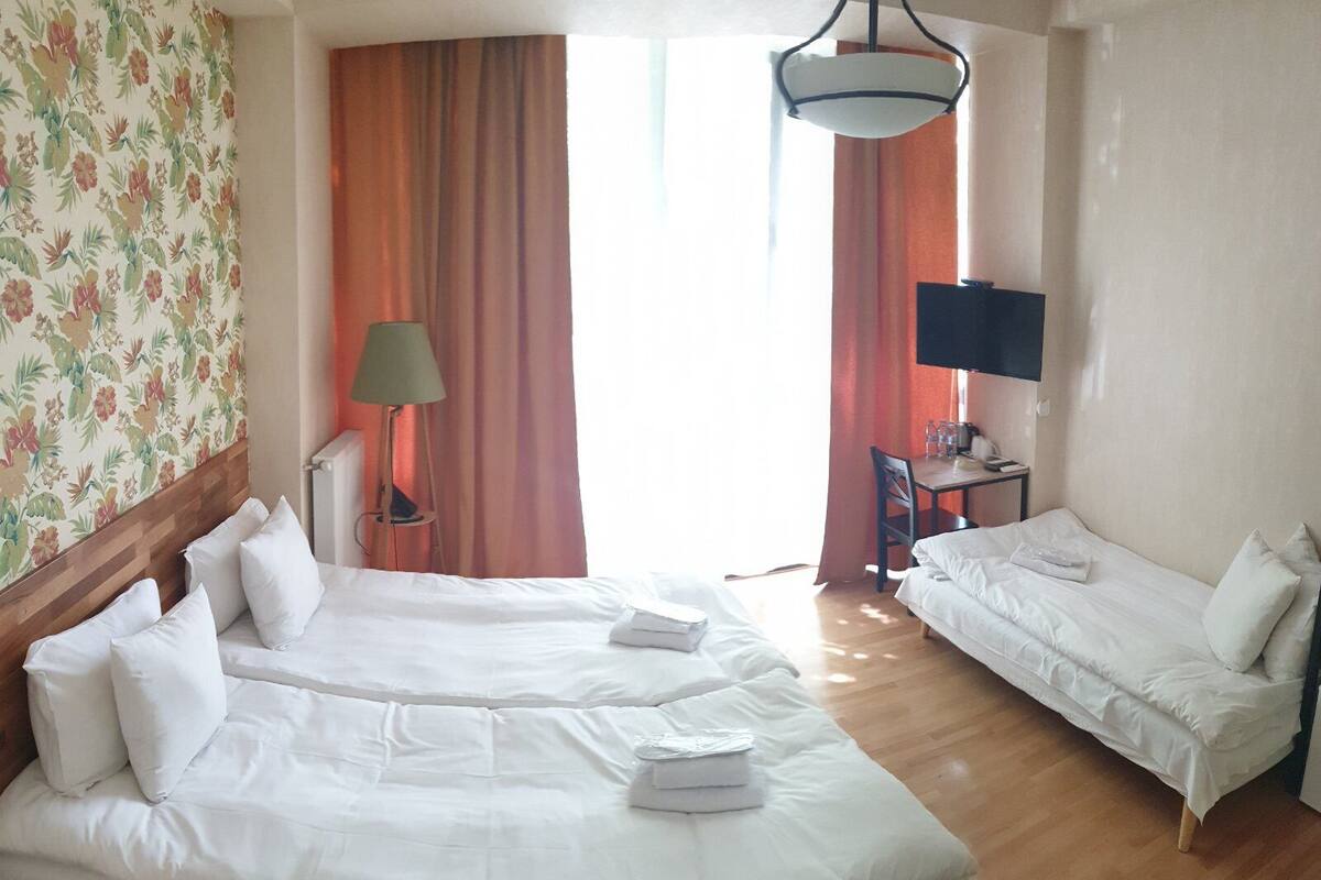 A hotel room with two beds, a desk with a chair, a TV, and a window with curtains.