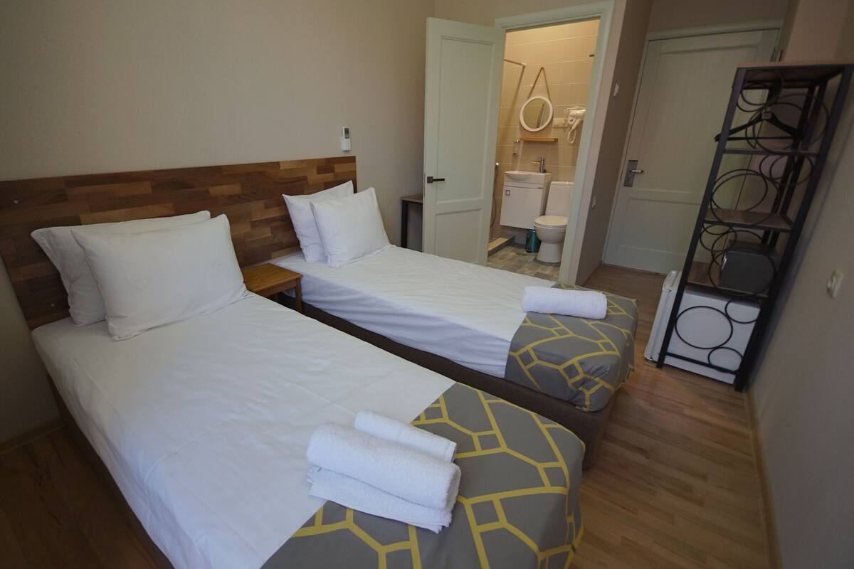 A hotel room with two beds, a wooden headboard, a bathroom with a toilet and sink, and a metal rack.