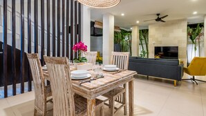 A dining area with a wooden table and chairs, a woven light fixture, a sofa, and a TV.