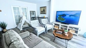 A living room with a sofa, two wicker chairs, a coffee table, a TV, and a bookshelf.