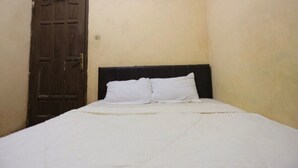 Ein Zimmer mit einem Einzelbett, einer Holztür und schlichten Wänden.