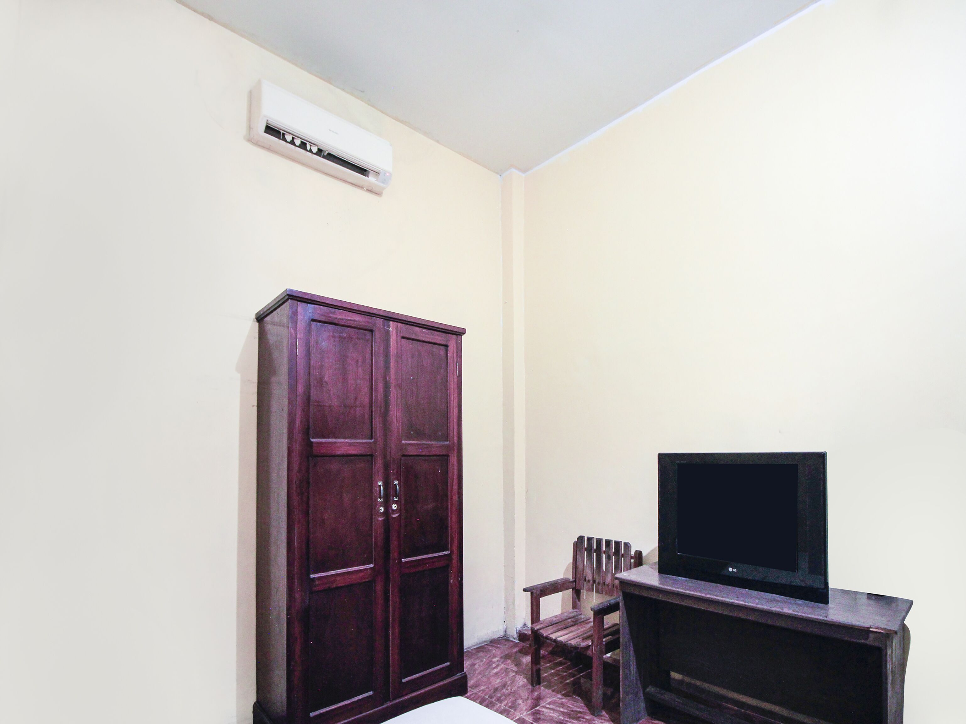 A room with a wooden cabinet, a television on a stand, and an air conditioning unit on the wall.
