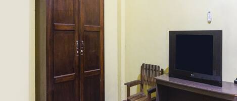 Una habitación con un armario de madera, un televisor sobre un mueble bajo y una silla.