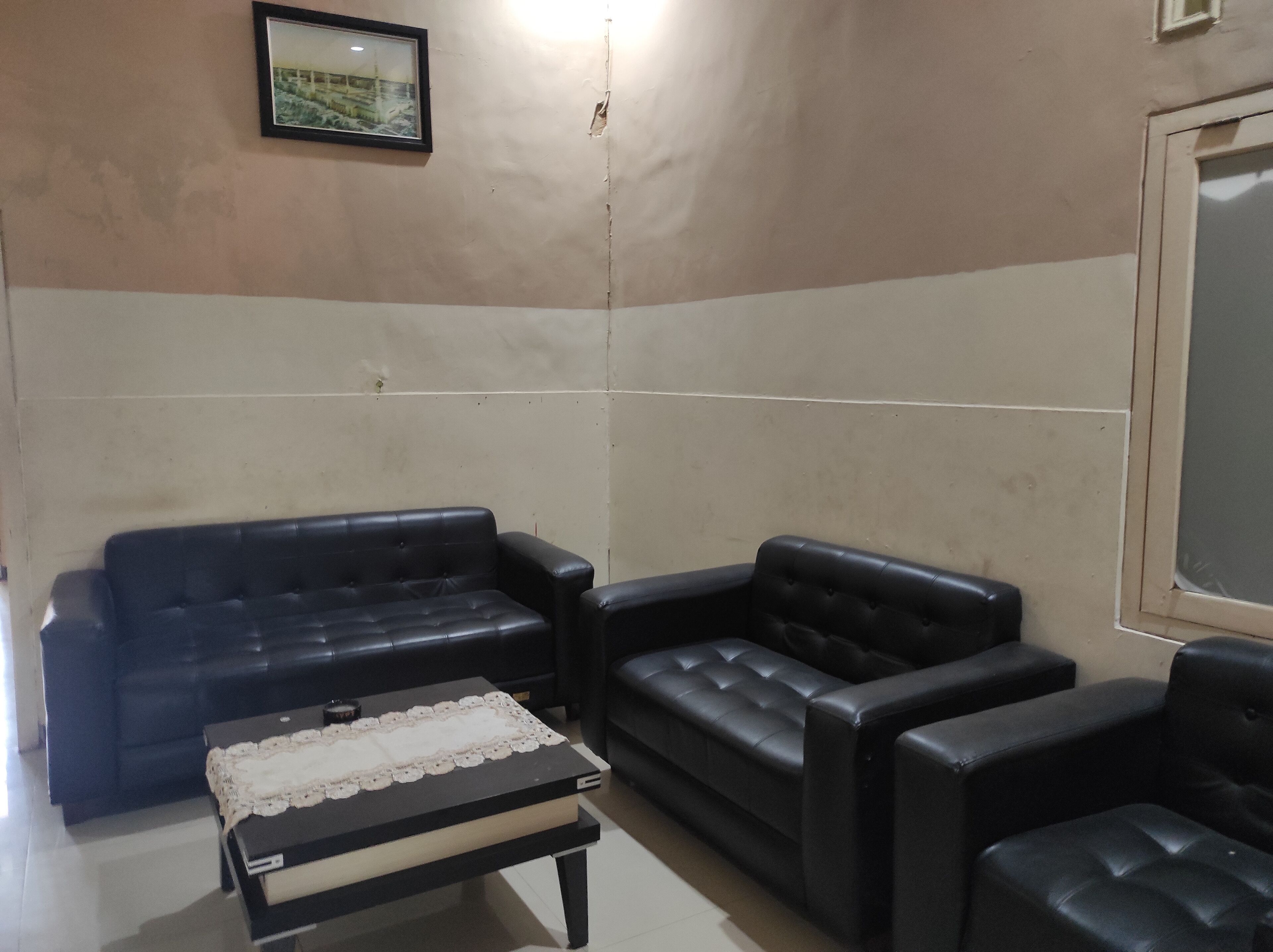 Un salon avec un canapé en cuir noir, un fauteuil assorti et une petite table recouverte d’une nappe en dentelle.