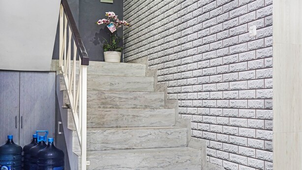 Un escalier avec des marches en marbre menant à un palier, un mur en briques et deux grands récipients d’eau sur la gauche.