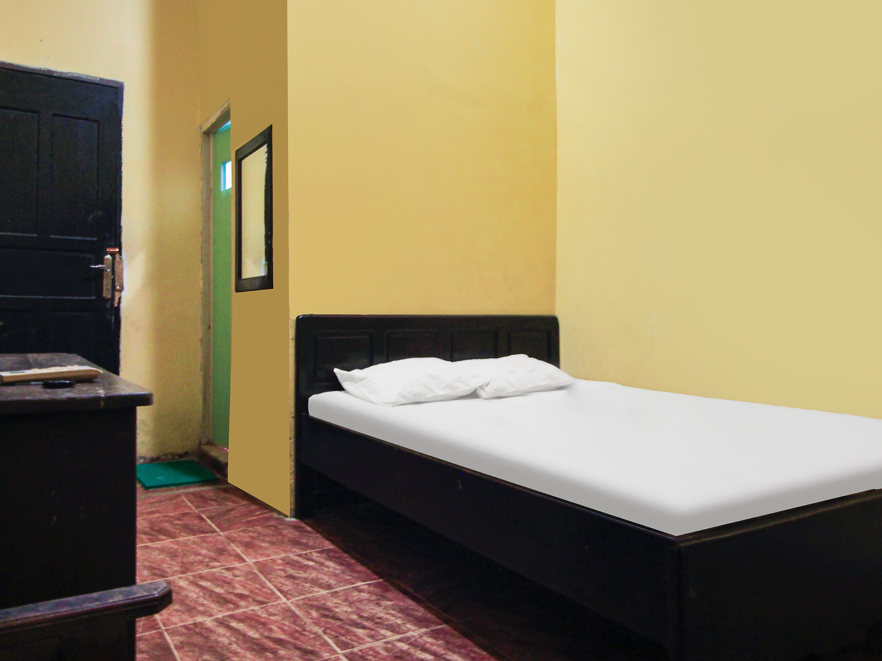 A small, single-bed room with a wooden headboard, a green door, and a tiled floor.