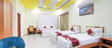 A hotel room with two beds, a dining table with fruit, a blue chair, and a TV on the wall.