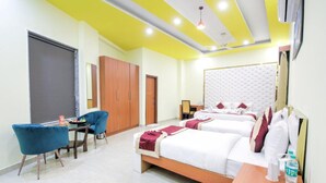 A hotel room with two beds, a desk with chairs, and a wardrobe. - Amit House (Greater Noida)
