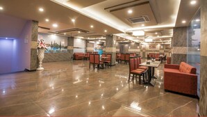A spacious lobby with a polished marble floor, multiple seating areas including sofas and tables, and a reception desk with a decorative vase. - Amit House (Greater Noida)