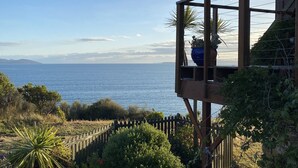 A wooden deck with a view of the sea, surrounded by greenery and a stone pathway. - Waterfront beach house overlooking one of Tassie's favourite surf breaks (Dodges Ferry)