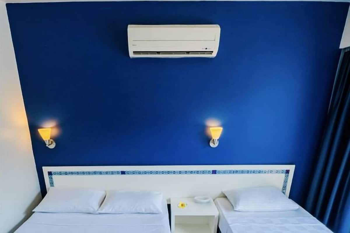 A hotel room with two single beds, a nightstand, an air conditioning unit, and wall-mounted lamps.