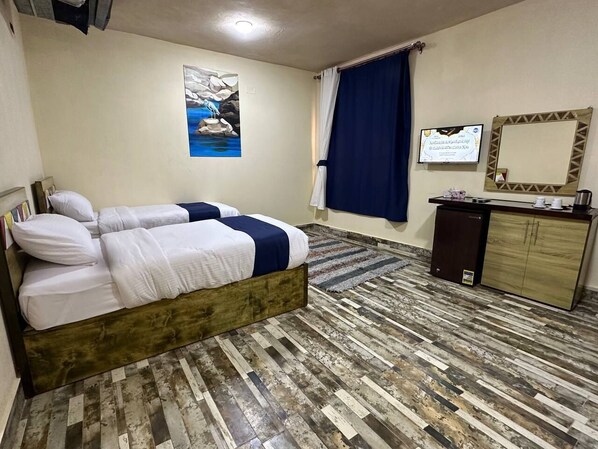 Une chambre avec un lit, un bureau, un petit réfrigérateur, un miroir et un tableau accroché au mur.