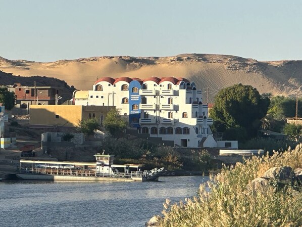 A coastal building with multiple levels and arched windows, situated near a body of water with a boat docked in front.