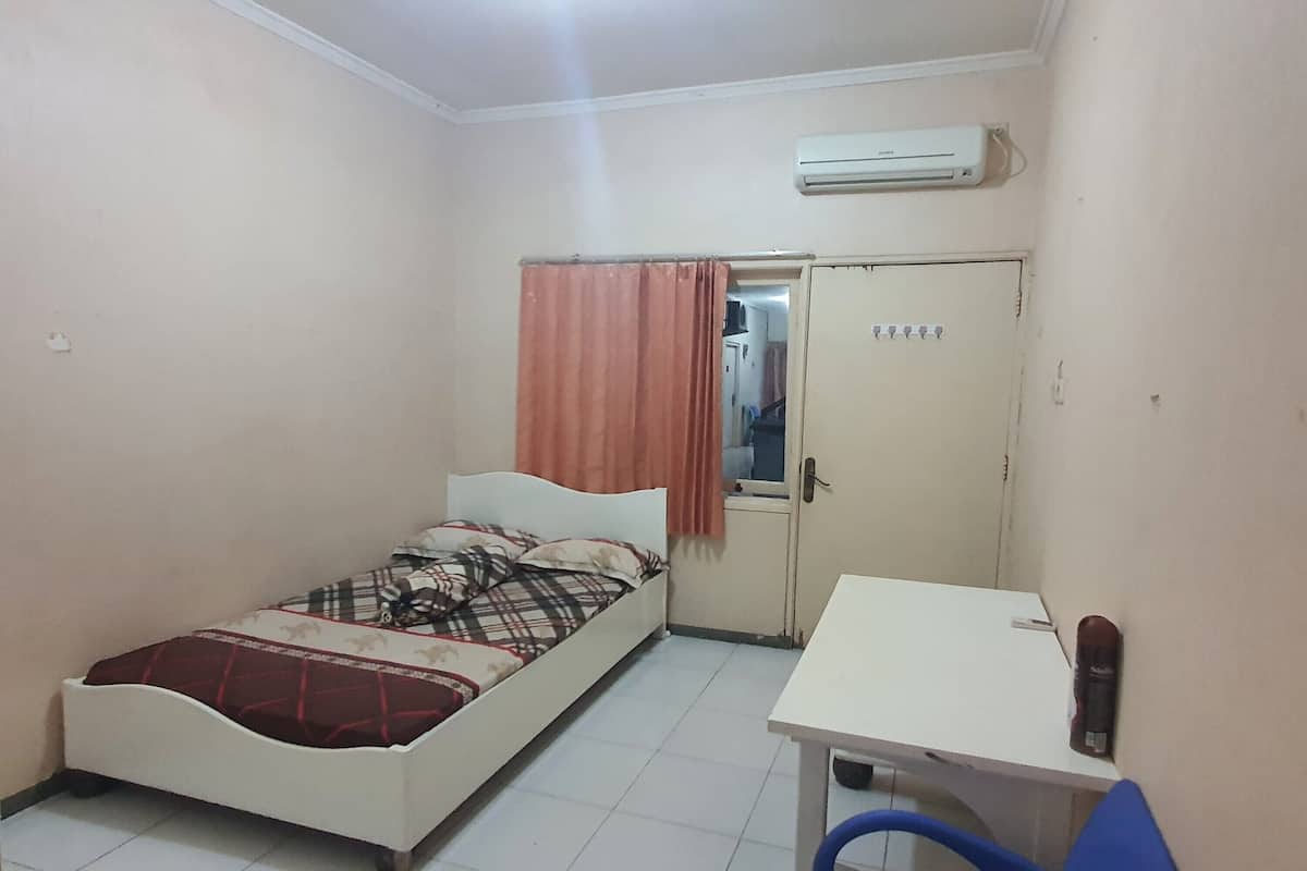 Une petite chambre avec un lit simple, un bureau et une chaise, un climatiseur et une porte avec une fenêtre.