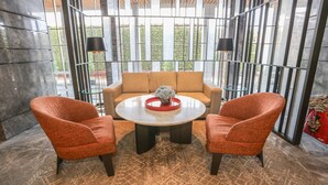 A modern interior with a round table, two orange chairs, a beige sofa, and a patterned rug. - OYO 93447 City Rooms Apartment (Tangerang)