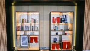 Two illuminated bookshelves with books and decorative items, set against a wooden wall with a marble floor. - OYO 93447 City Rooms Apartment (Tangerang)