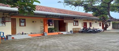 A building with a tiled roof, a porch with a bench, and a motorcycle parked outside.