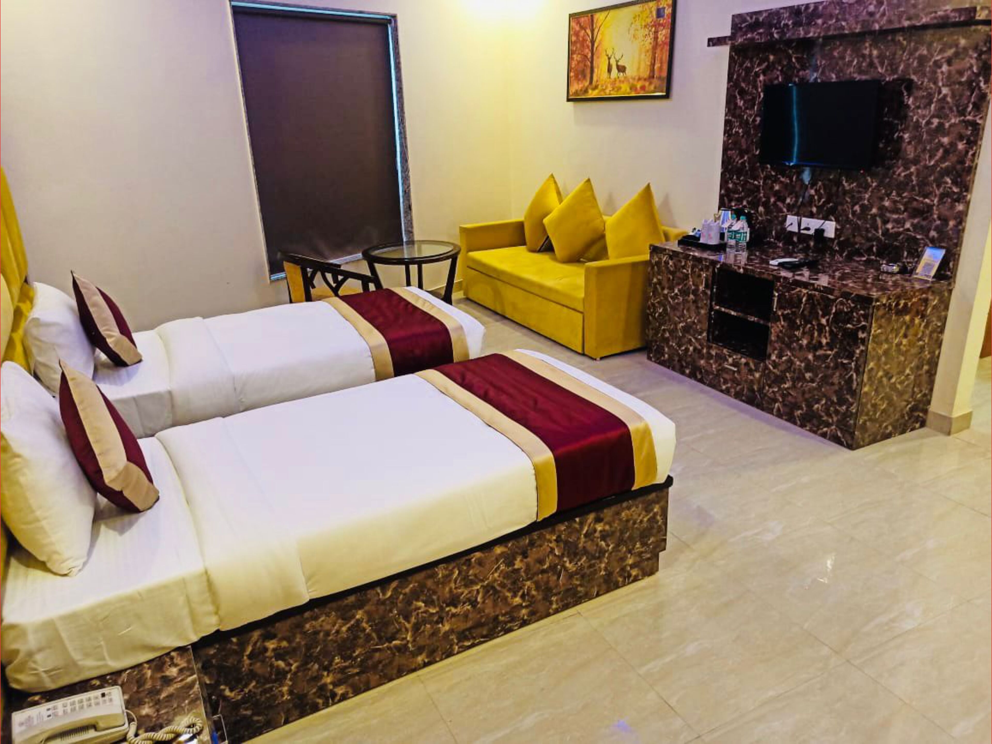 A hotel room with two beds, a yellow sofa, a small table, a TV, and a marble reception desk.