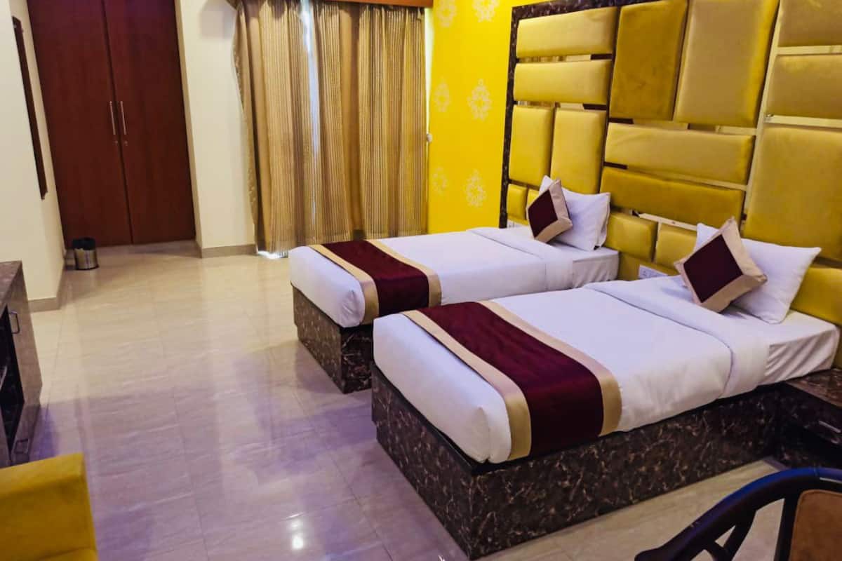 A hotel room with two beds, a wooden wardrobe, a curtain, and a yellow accent wall.