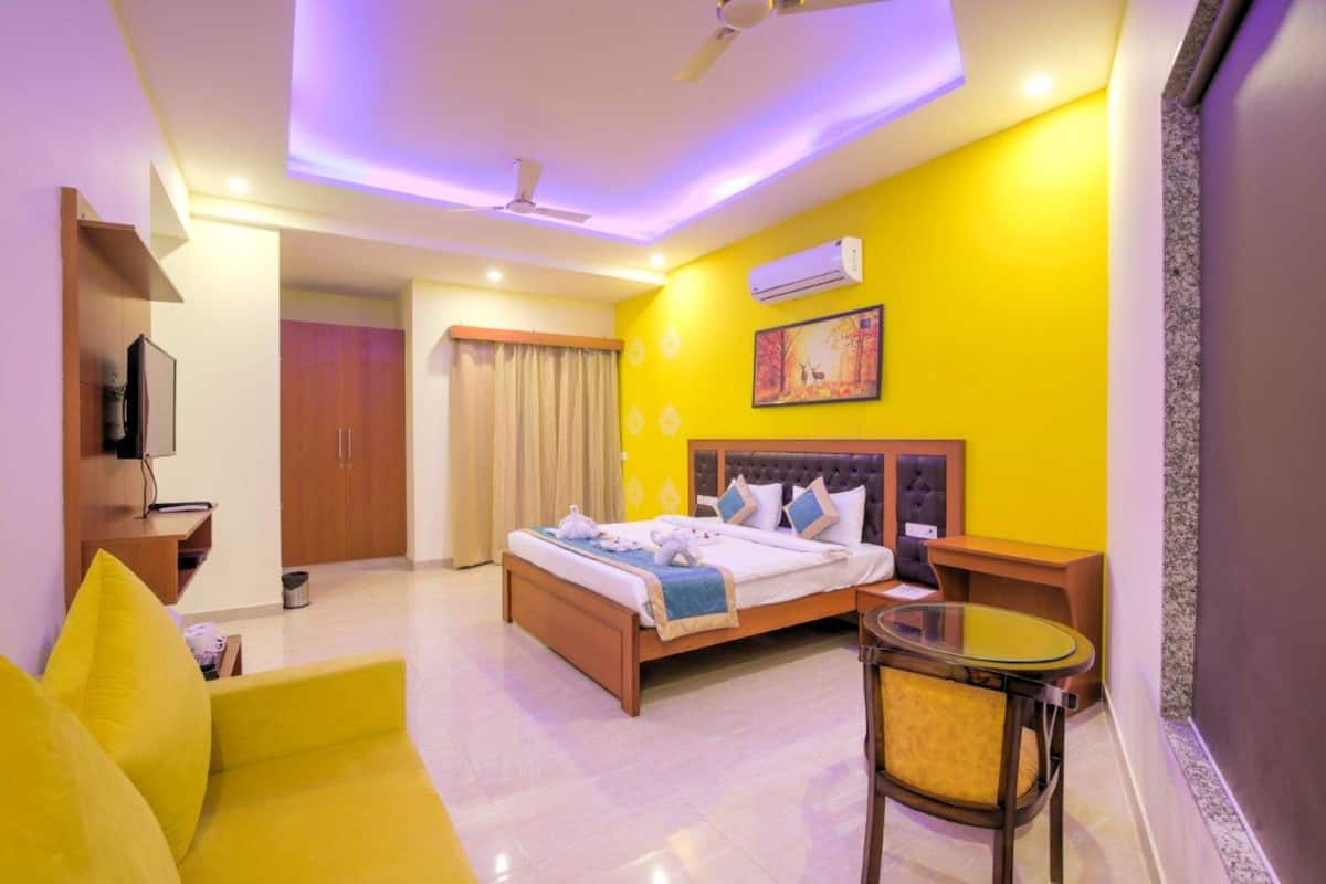 A hotel room with a bed, a small table, a sofa, and a ceiling fan.