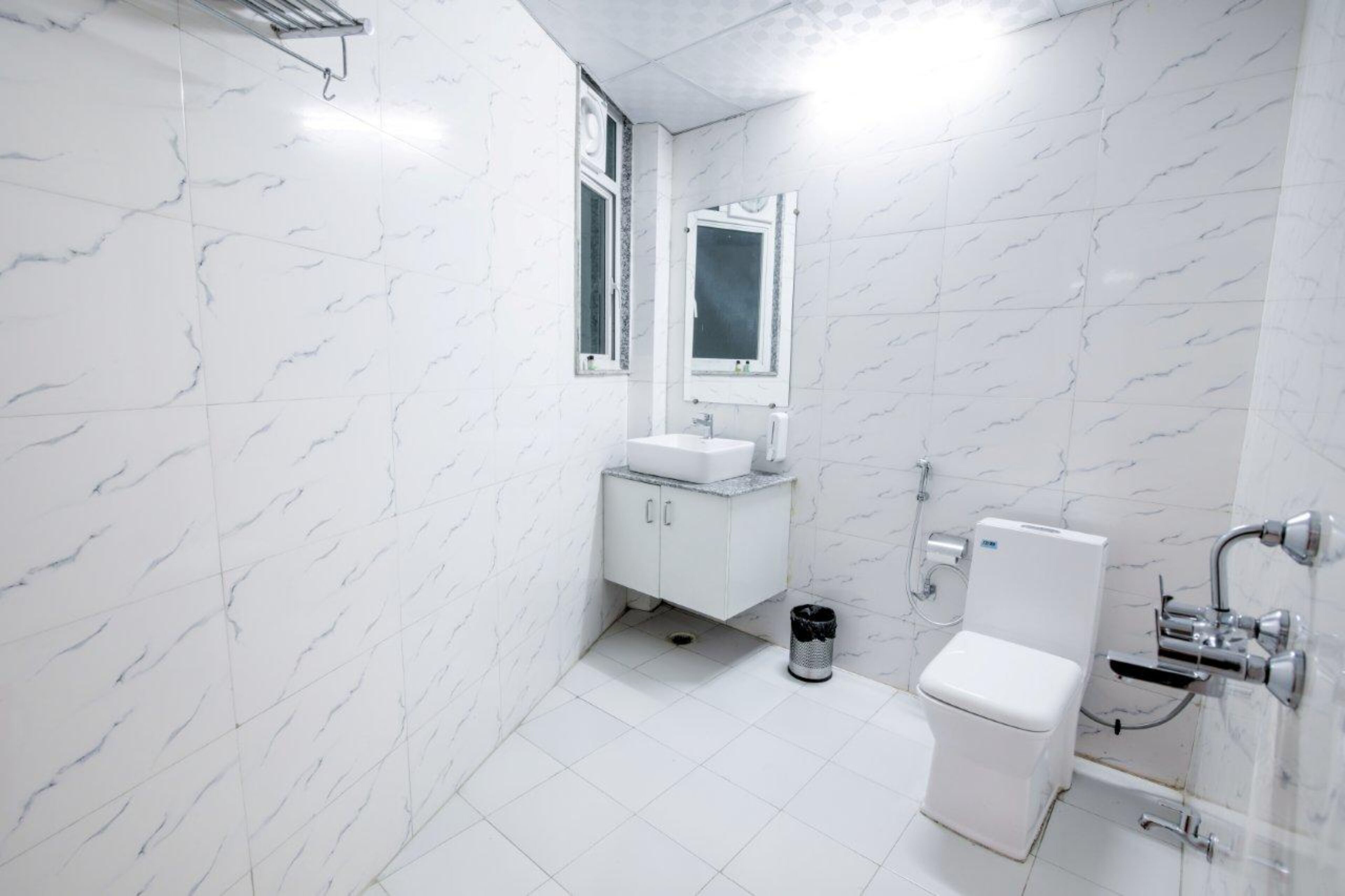 A small, modern bathroom with white marble walls, a white sink, a toilet, and a shower.