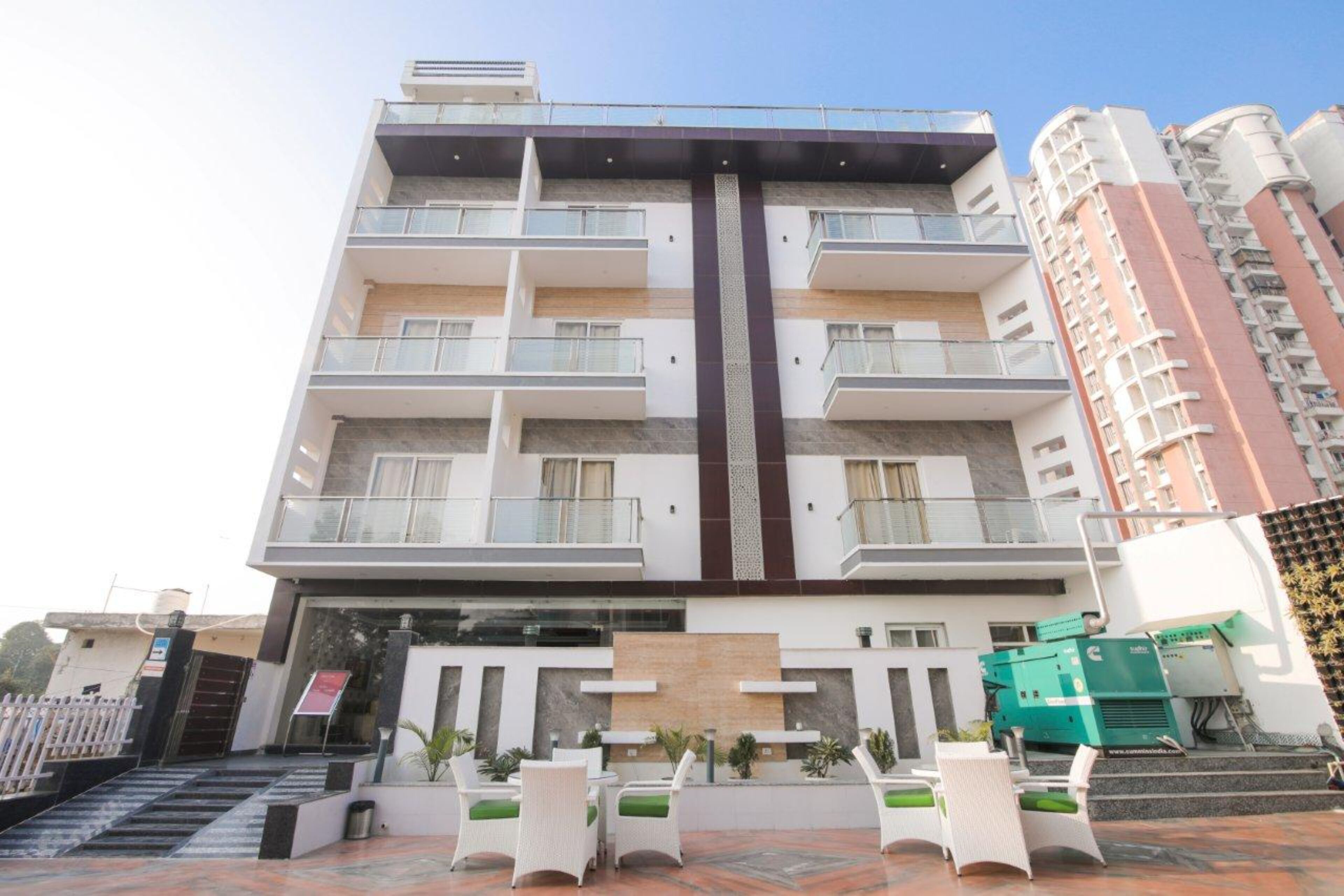 Un hotel de varios pisos con balcones, un elemento vertical central y mobiliario para exteriores.
