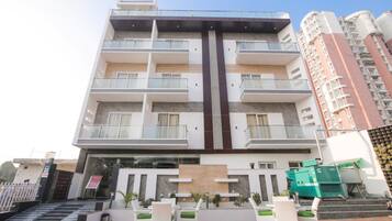 Un hotel de varios pisos con balcones, un elemento vertical central y mobiliario para exteriores.
