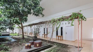 A corridor with a garden area, including a small water feature, wooden benches, and potted plants. - Hotel O Wisma Silampari (Lubuklinggau)