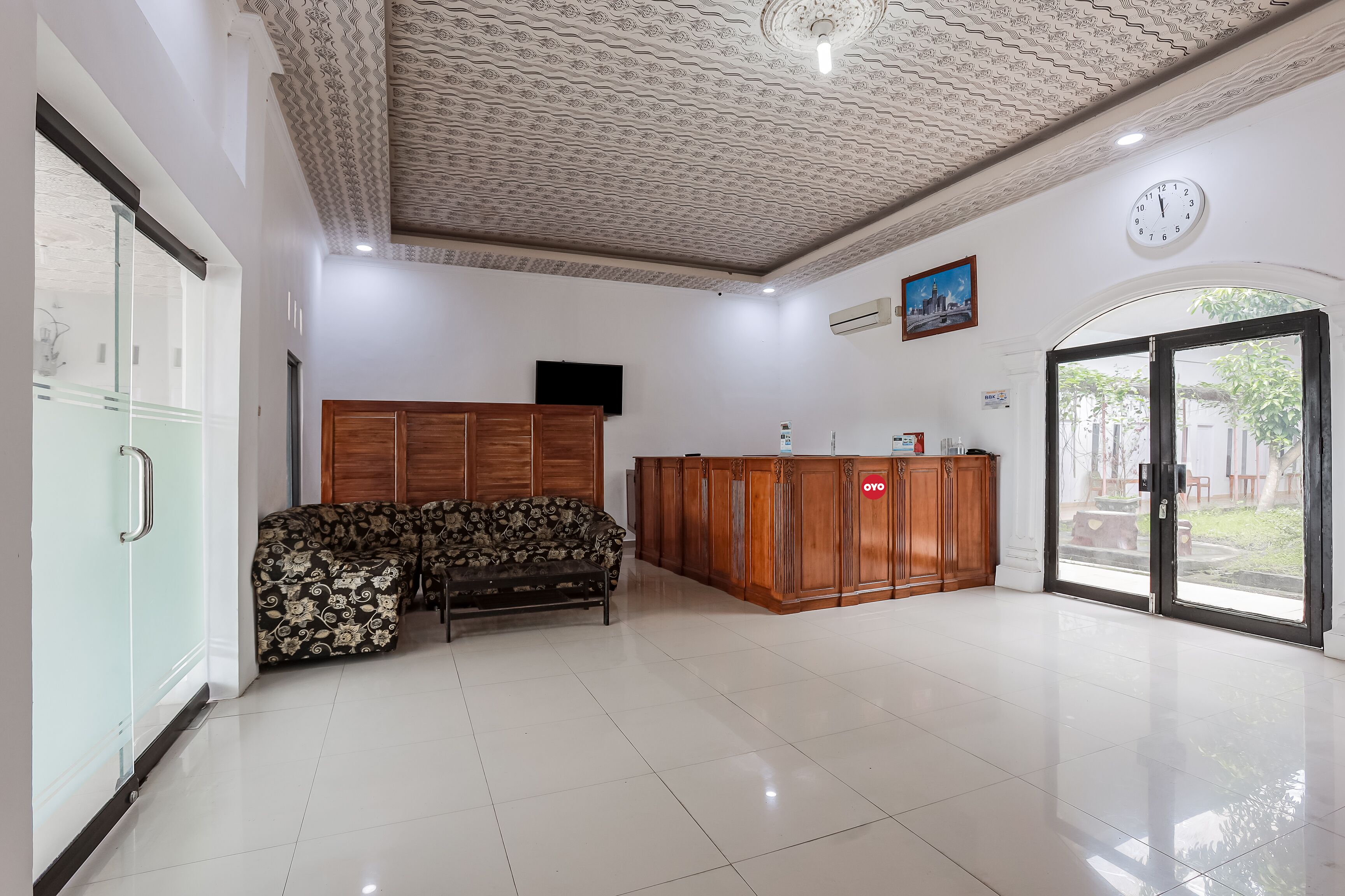 A spacious room with a patterned ceiling, a sofa, a wooden cabinet, and a clock on the wall.