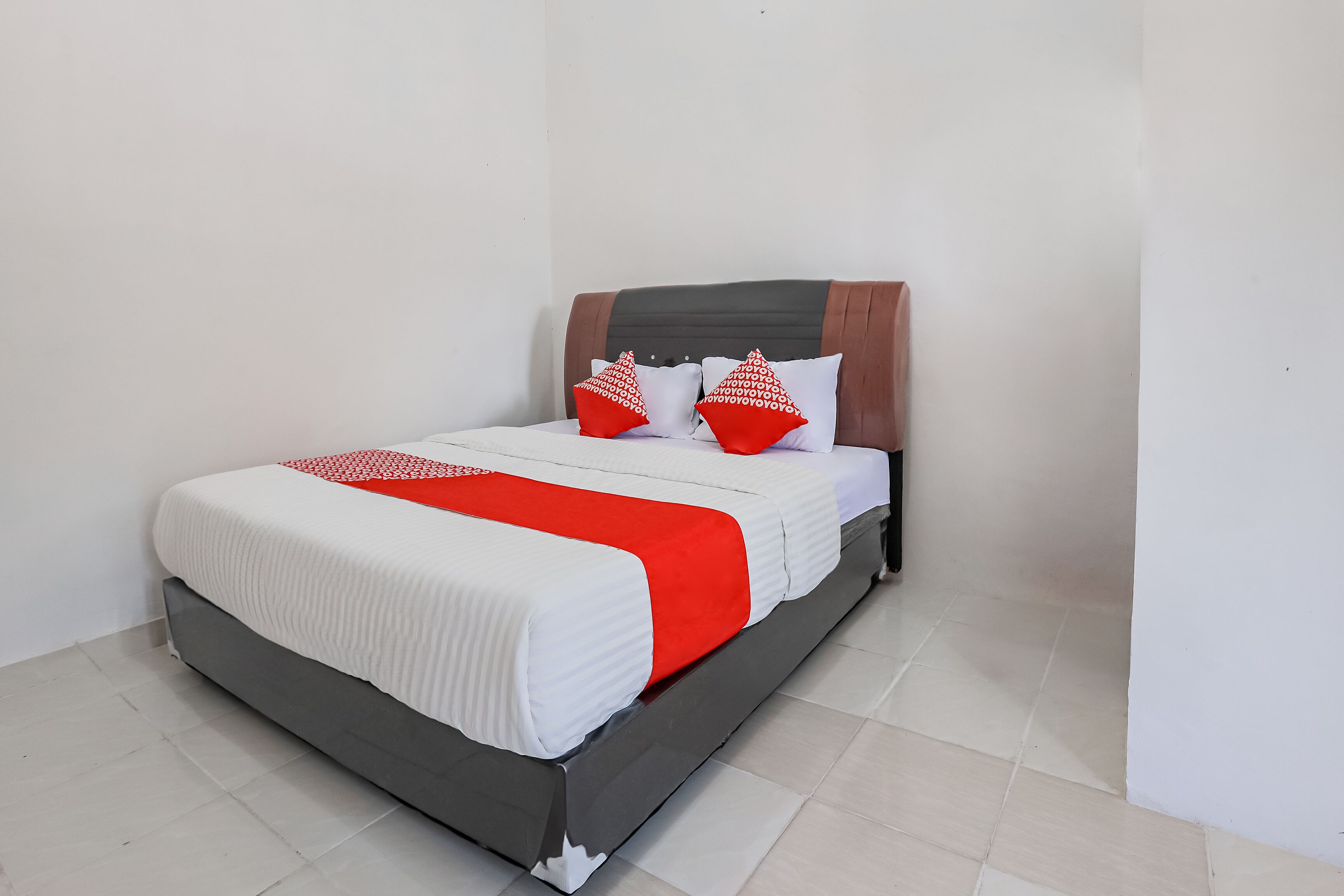 Een bed met een wit-rode spreideken, twee rode kussens en een houten hoofdbord.