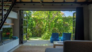 Un espace de vie ouvert avec vue sur un jardin luxuriant, comprenant un canapé, une table basse et un téléviseur diffusant du contenu de « Netflix ».