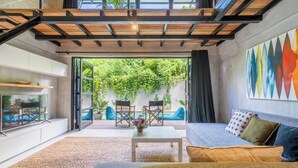 Un salon moderne avec un canapé, une table basse et des fauteuils. Une grande fenêtre offre une vue sur la verdure et une piscine à l’extérieur.