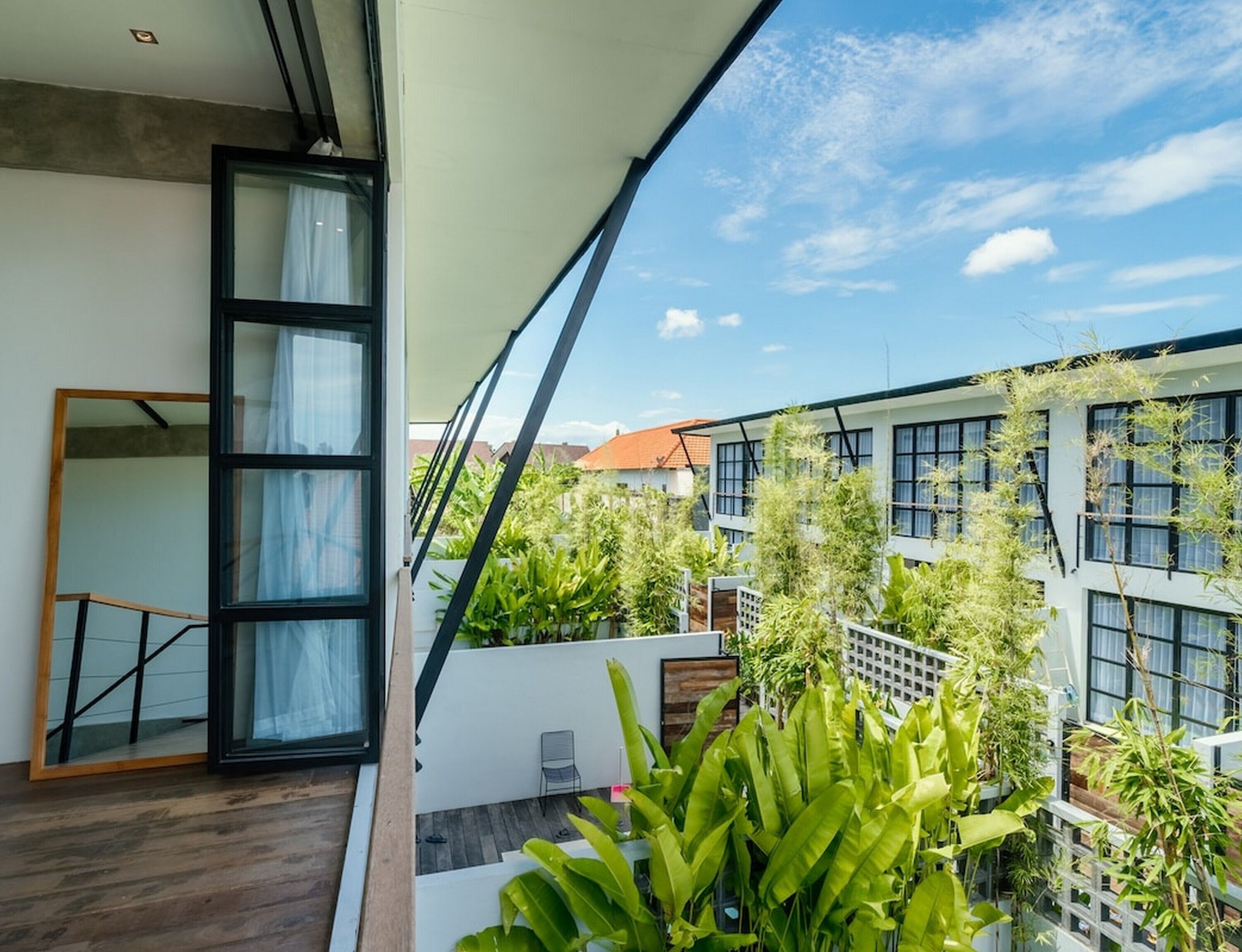 A modern balcony with a wooden floor, a glass door, and a view of neighboring buildings and greenery.