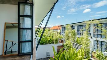 A modern balcony with a wooden floor, a glass door, and a view of neighboring buildings and greenery.