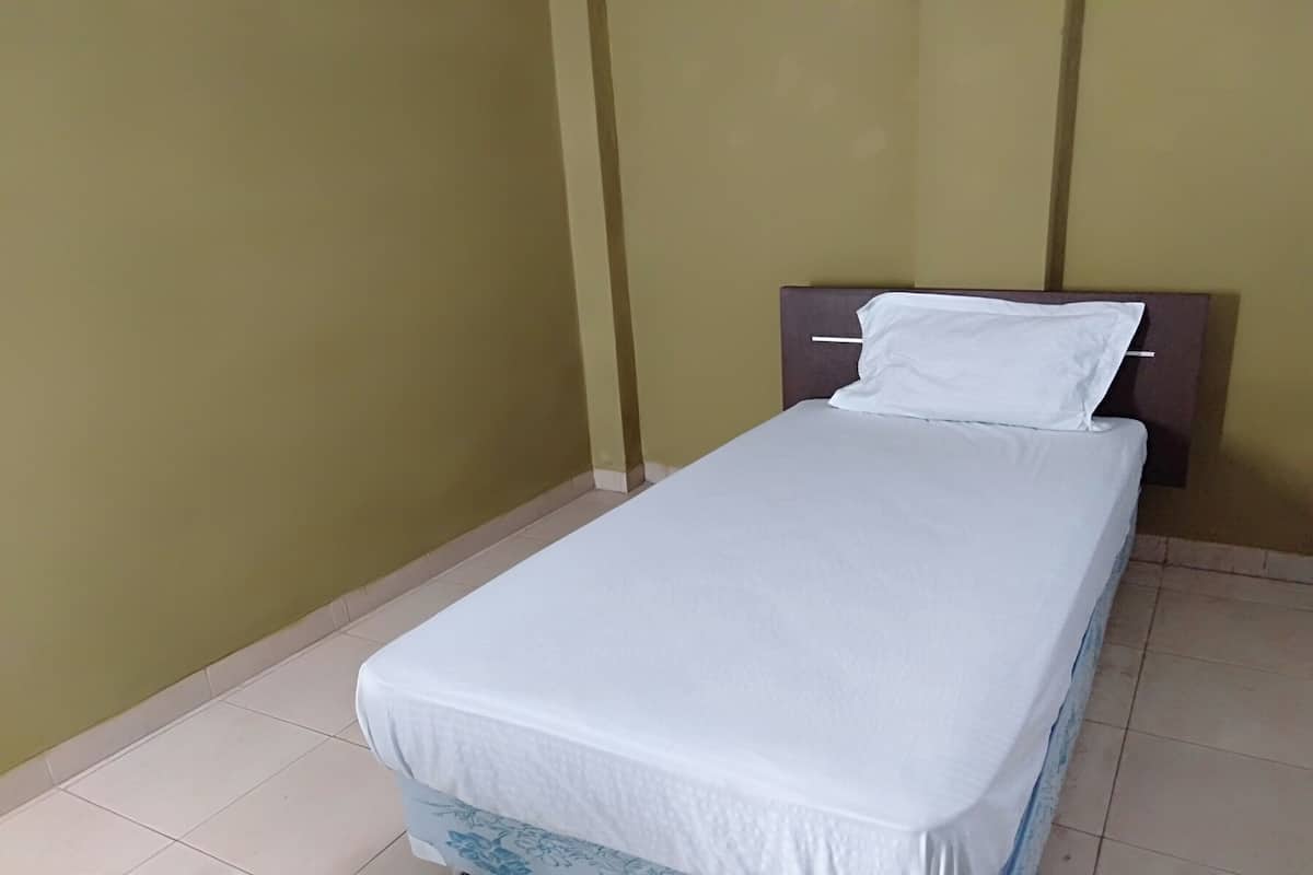A single bed with a white mattress and matching pillow in a room with plain walls and tiled flooring.
