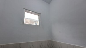Una habitación con una ventana pequeña, paredes blancas y una sección inferior con diseño de mármol.