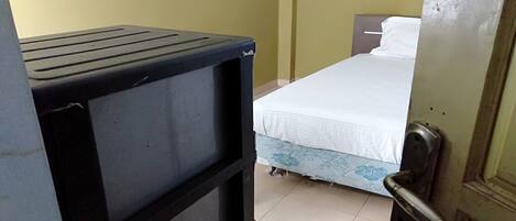 A room with a bed, a door, and a black object that appears to be a storage unit or furniture.