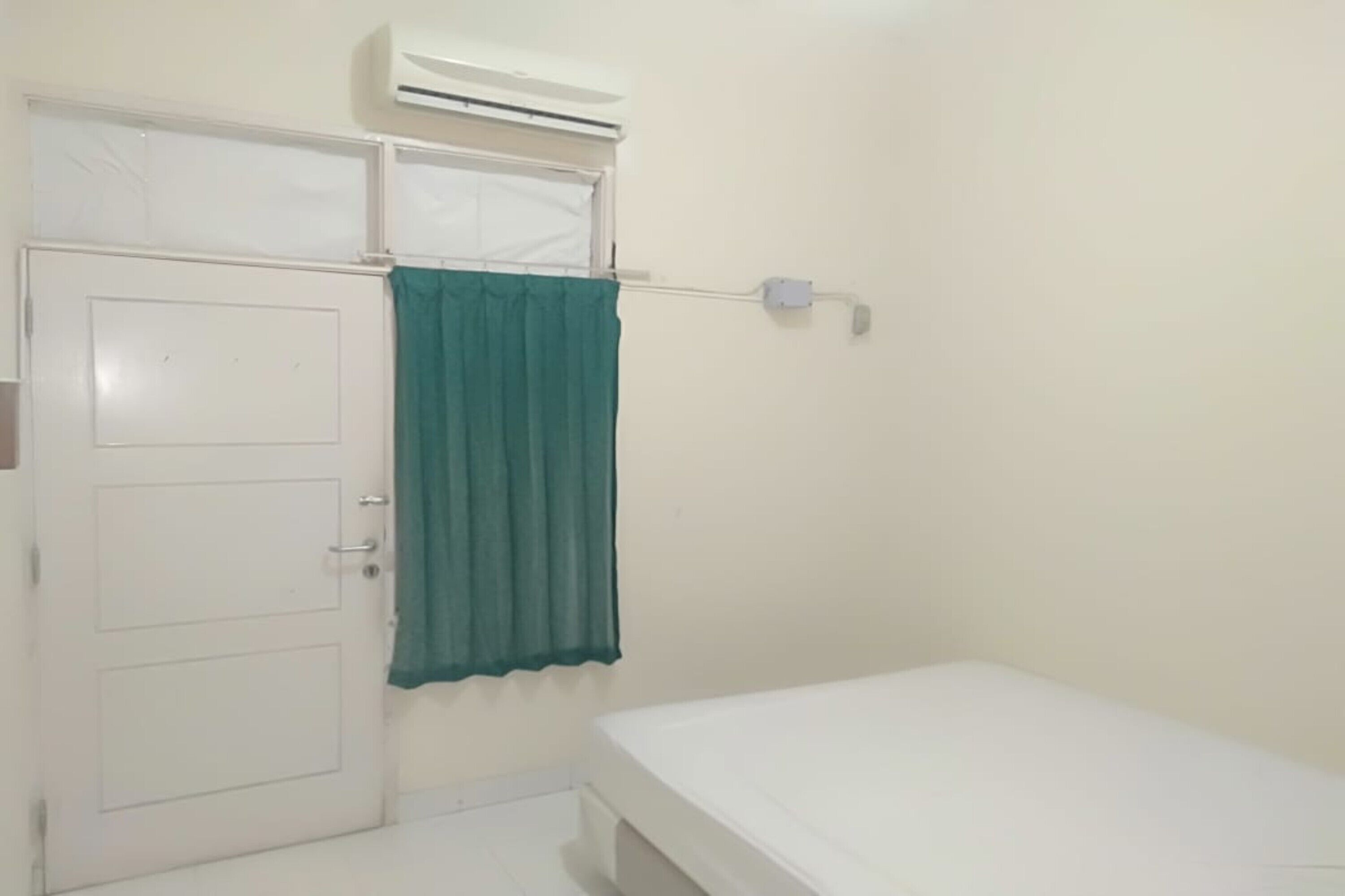 Habitació petita i neta amb un llit individual, un armari blanc i una cortina verda.