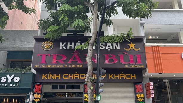 A hotel named "KHÃSÃN SAN TRÃN BÚI" with a neon sign, potted plants, and a motorcycle parked outside. - Tran Bui-242 Phan Xich Long-by BayLuxury (Ho Chi Minh City)
