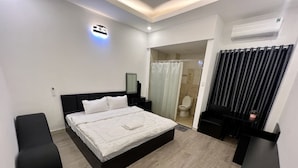 A modern hotel room with a large bed, a bedside table, a mirror, a shower area, and a black chair. - Tran Bui-242 Phan Xich Long-by BayLuxury (Ho Chi Minh City)