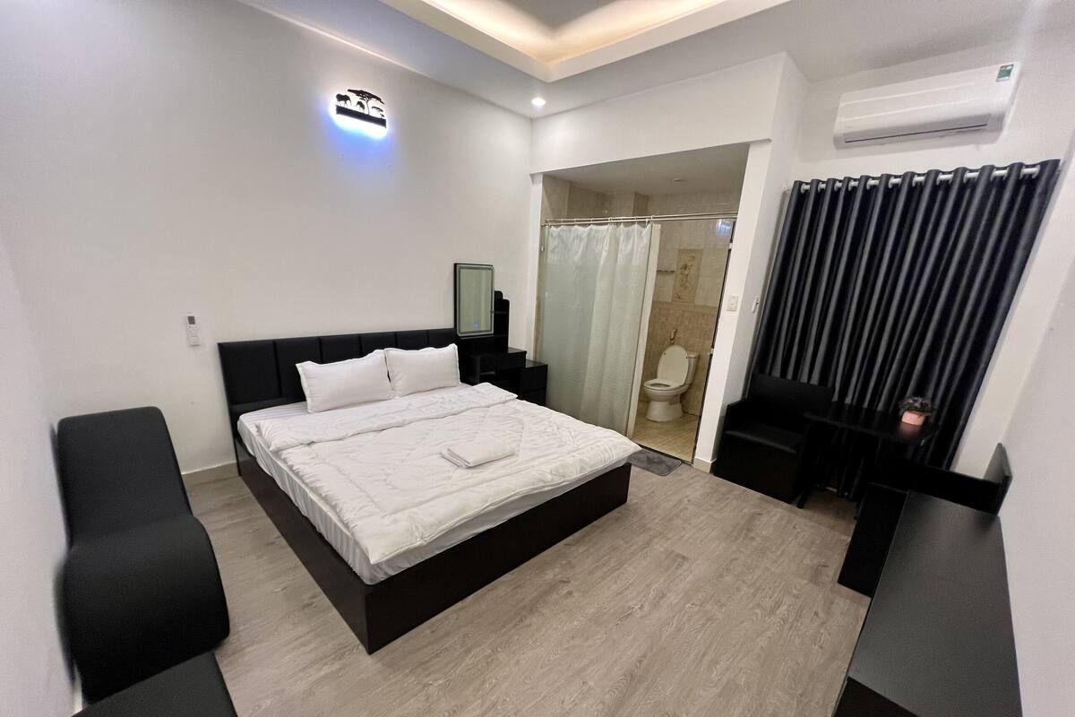 Ein modernes Hotelzimmer mit einem großen Bett, einem Nachttisch, einem Spiegel, einer Dusche und einem schwarzen Sessel.